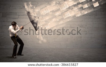 Business man protecting with umbrella against wind of papers concept