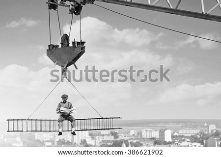 Relaxation needed. Black and white shot of a retro builder reading a newspaper sitting on a crossbar above the city Royalty-Free Stock Photo #386621902