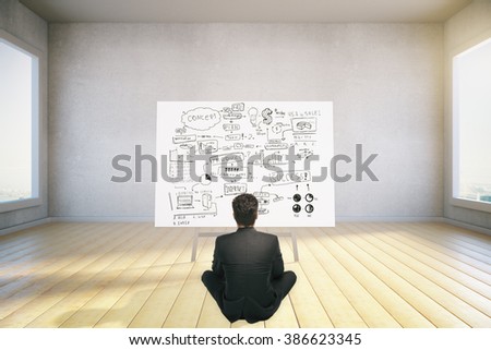 Businessman sitting in front of a board with business concept in a room with windows and wooden floor