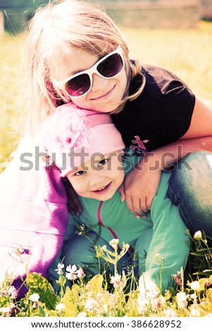 Little blond Caucasian sisters hugging in a sunny Summer day. Closeup portrait with tonal correction photo filter effect