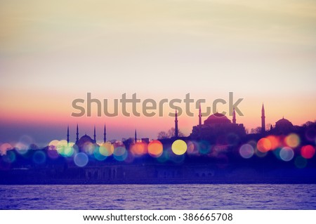Istanbul cityscape - mosque and minarets in the evening. Oriental blurry background - silhouettes of temples in ultraviolet colors and bokeh light effect. Landmarks of arabic culture in night lights. Royalty-Free Stock Photo #386665708