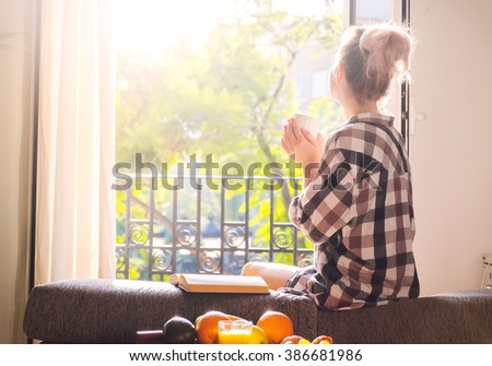 Young pretty woman  sitting at opened window drinking coffee and looking outside enjoys of rest Royalty-Free Stock Photo #386681986
