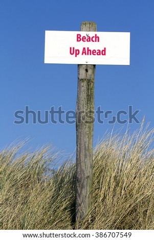 Wooden Pole with White Sign Board Saying Beach Up Ahead in the Dunes with a Blue Sky Background