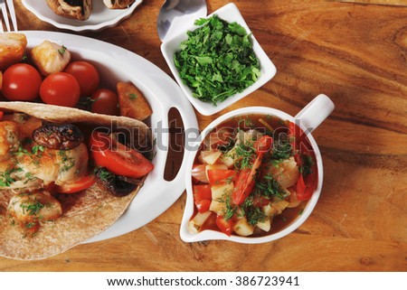 big mexican taco served with soup, fresh vegetables , baked mushroom with teriyaki sauce , on white crockery plates over wooden table with green staff