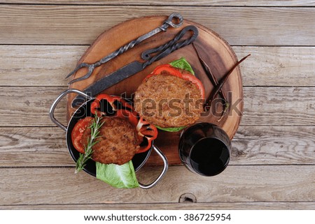 fresh grilled beef huge hamburger served on wood plate with red wine glass chili pepper rosemary green salad leaf and forged vintage antique cutlery over wooden table empty space for text