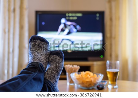 Watching tennis match on TV set (television) with feet on table and eating snacks  stock photo
