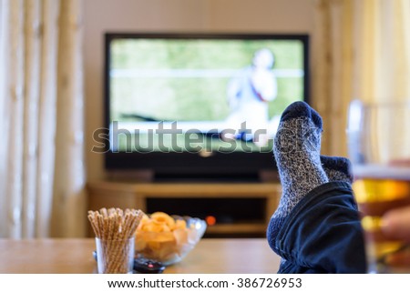 Watching tennis match on TV set (television) with feet on table and eating snacks stock photo