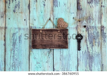 Blank rustic sign with rope heart and house key hanging on antique teal blue wood background