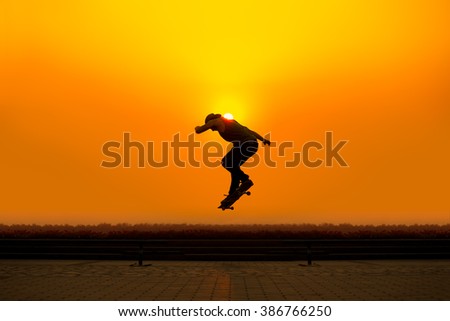silhouette young man playing skateboard with height jump in evening time with sunset yellow orange background