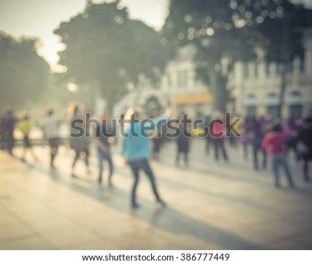 Blur background group of people dancing a fitness dance or line dancing/aerobics at Ly Thai To Park Hanoi, Vietnam. Healthy lifestyle concept. Nature outdoor workout.Beautiful early morning warm light