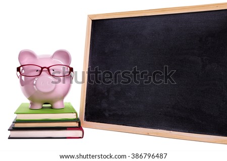Piggybank wearing glasses on small stack of books, blank blackboard, college education success concept