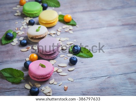Air cake macaroon green, pink, cream, yellow, purple on white wooden background nuts almonds, blueberries and cape gooseberry, mint, empty space for your text


