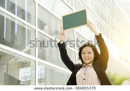 Portrait of a young Asian business woman smiling and holding a blank sign board, standing at office environment, beautiful golden sunlight background.