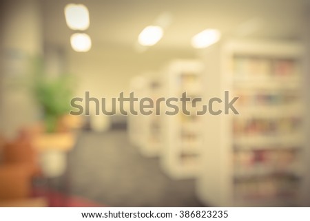 Blurred abstract background of public library interior with bookshelf aisle full of textbooks, literature and seating for students, faculties for reading. Self-study, educational concept/background.