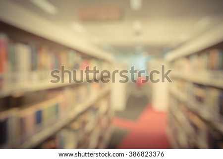 Blurred abstract background of public library interior with bookshelf aisle full of textbooks, literature and magazines. Female student is selecting books from bookshelf. Self-study education concept.