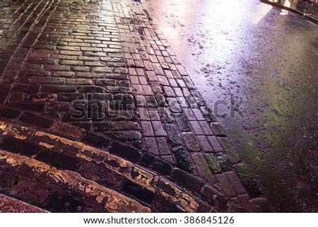 Looking Down at Wet Street and Sidewalk with Combination of Pavement and Cobblestones - High Angle View of Street at Night After Rain Shower from Rounded Curb