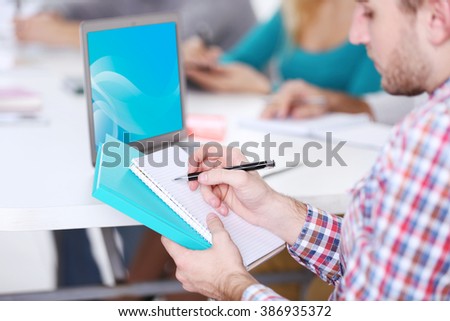 Young man sitting and making notes at the office meeting