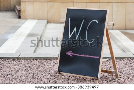 WC and arrow symbol on blackboard outdoors
