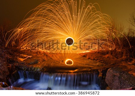 Sparks from the burning steel wool reflected in a creek near a waterfall
