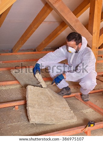 Worker cutting mineral wool panel installing thermal insulation on a building