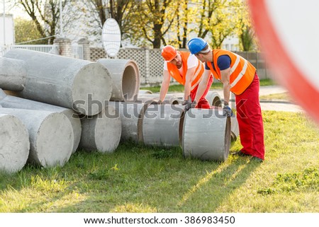 Photo of construction workers rolling big concrete pipes