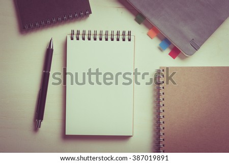 Opened notebook with blank area for text or message, grey, blank, and brown closed notebook on wood table with vintage filter effect