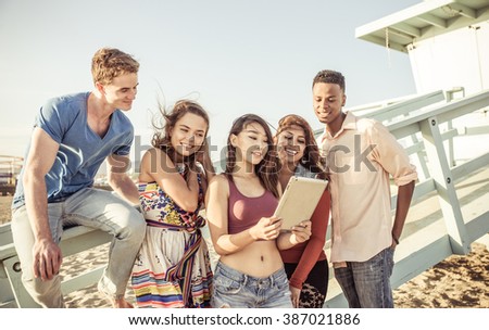 Mixed race group of friends enjoying time together on the beach watching funny videos on the social networks