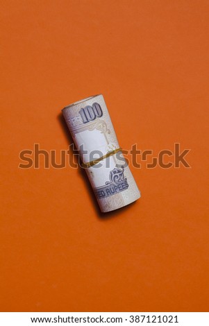 Roll of indian currency shot from above against an orange background.