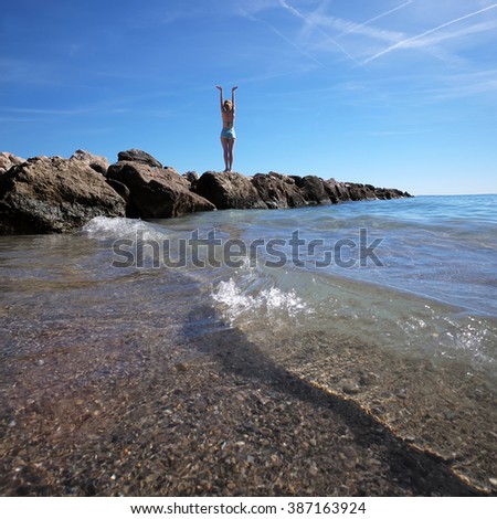 Photo closeup of one person young girl exercising lifting hands to blue sky on wet stone at seashore with clear waves and white spindrifts running on seascape background, square picture