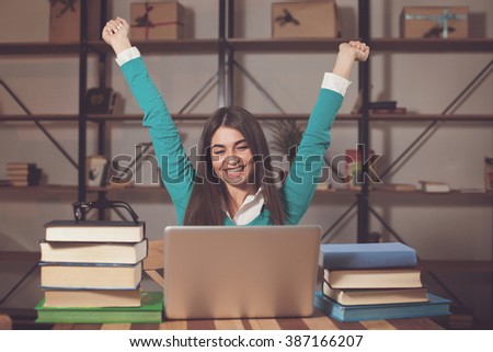 Woman is happy about her successful work with laptop at the table