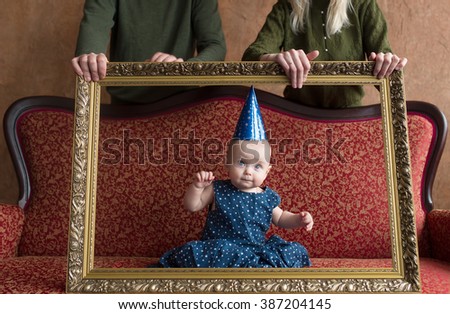 Birthday of the little girl. She sits on a red sofa and looks out of a picture frame.