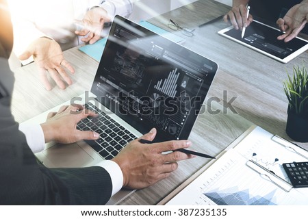 business documents on office table with smart phone and laptop computer and graph financial with social network diagram and three colleagues discussing data in the background