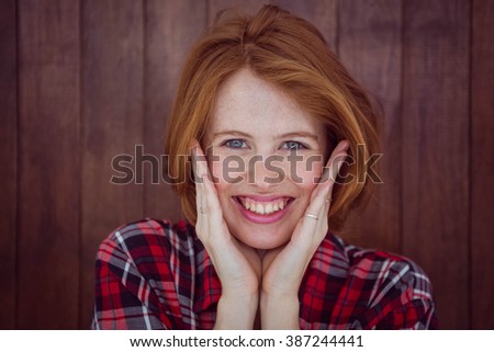smiling hipster woman with her hands on her face against a wooden background