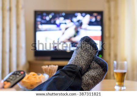 man watching professional wrestling match on TV (television) with feet on table, eating snacks - stock photo
