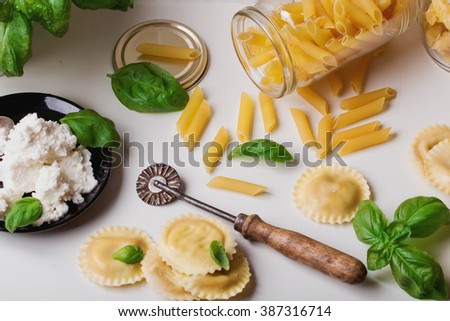 Home made ravioli, penne and fusilli pasta with fresh basil, ricotta cheese with pasta cutter over the white table with kitchen tiles background