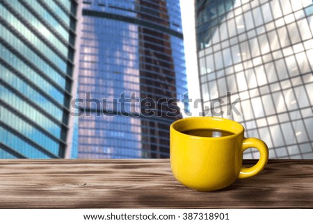 Coffee in cup on wooden table opposite a defocused cityscape for background. Collage. Selective focus.