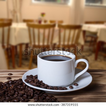 Coffee beans and coffee in white cup on wooden table opposite a defocused the interior of the museum's room for background. Collage. Selective Focus.