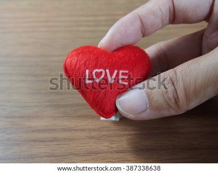 Holding little pillow with red heart shape and love word on wood background