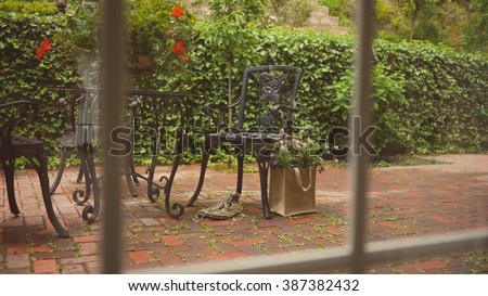 A bag of clover flowers and old shoes next to a patio chair after rain. View through the window.  