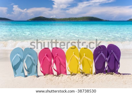 beach flip flops in rainbow color pattern on tropical sand