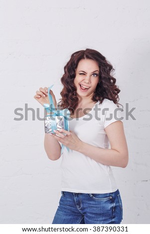 Young cute girl winks and unpacks a gift. Human emotions. Girl in a white T-shirt.