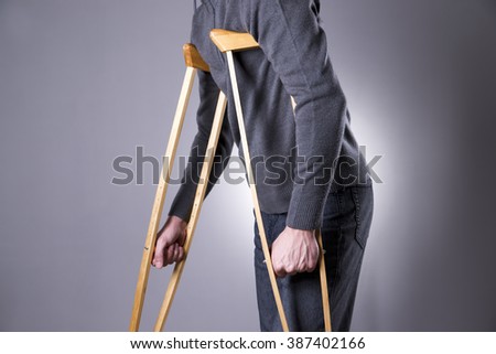 Man on crutches on a gray background. Studio shot Royalty-Free Stock Photo #387402166