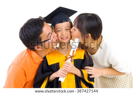 Asian kindergarten child in graduation gown and mortarboard kissed by her parent during graduation Royalty-Free Stock Photo #387427144