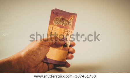 Retro styled or retro color hand holding, counting or giving away Ringgit Malaysia currency bank notes. Concept of bribery and monetary profit. Slightly de-focused and close-up shot. Copy space.