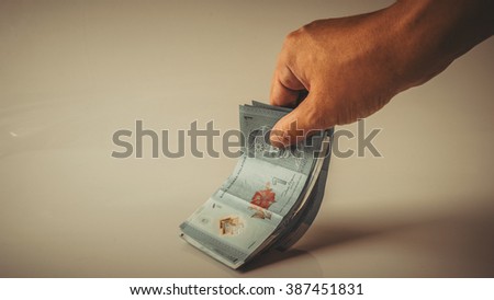 Retro styled or retro color hand holding, counting or giving away Ringgit Malaysia currency bank notes. Concept of bribery and monetary profit. Slightly de-focused and close-up shot. Copy space.