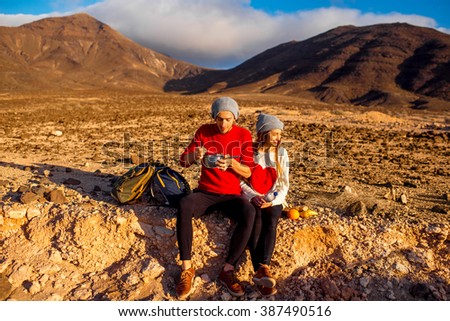 Young couple travelers eating healthy food from cooking pan sitting on the ground on desert mountain landscape background. 