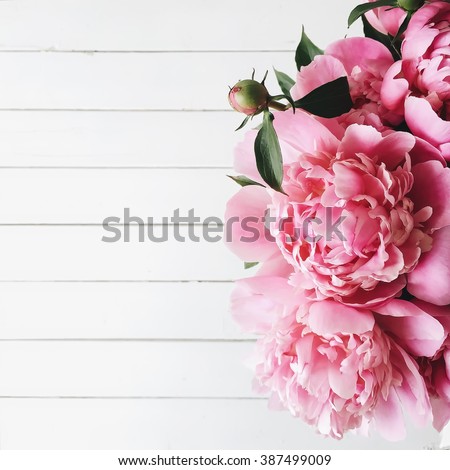 Overhead view of bouquet of pink peonies on white wooden background