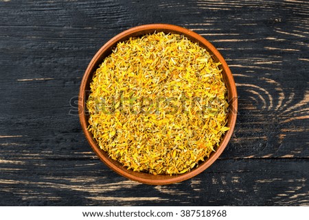 Bowl full of dried calendula flowers on a wooden background top view