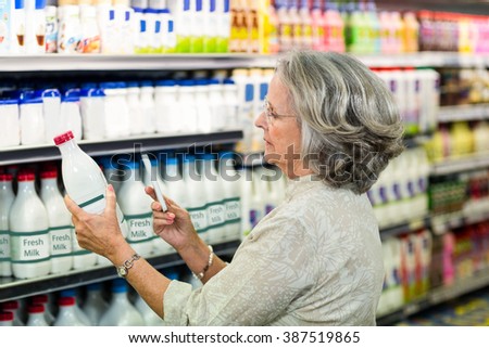 Senior woman taking picture of milk bottle at the supermarket