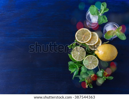Lime, mint, lemon and vodka on a blue  wooden table. Party time. Toned image. Selective focus. Yellow, green, ice.